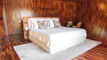 Quarto moderno com uma cama grande, paredes de madeira, um tapete branco e uma pequena mesa com cadeiras.