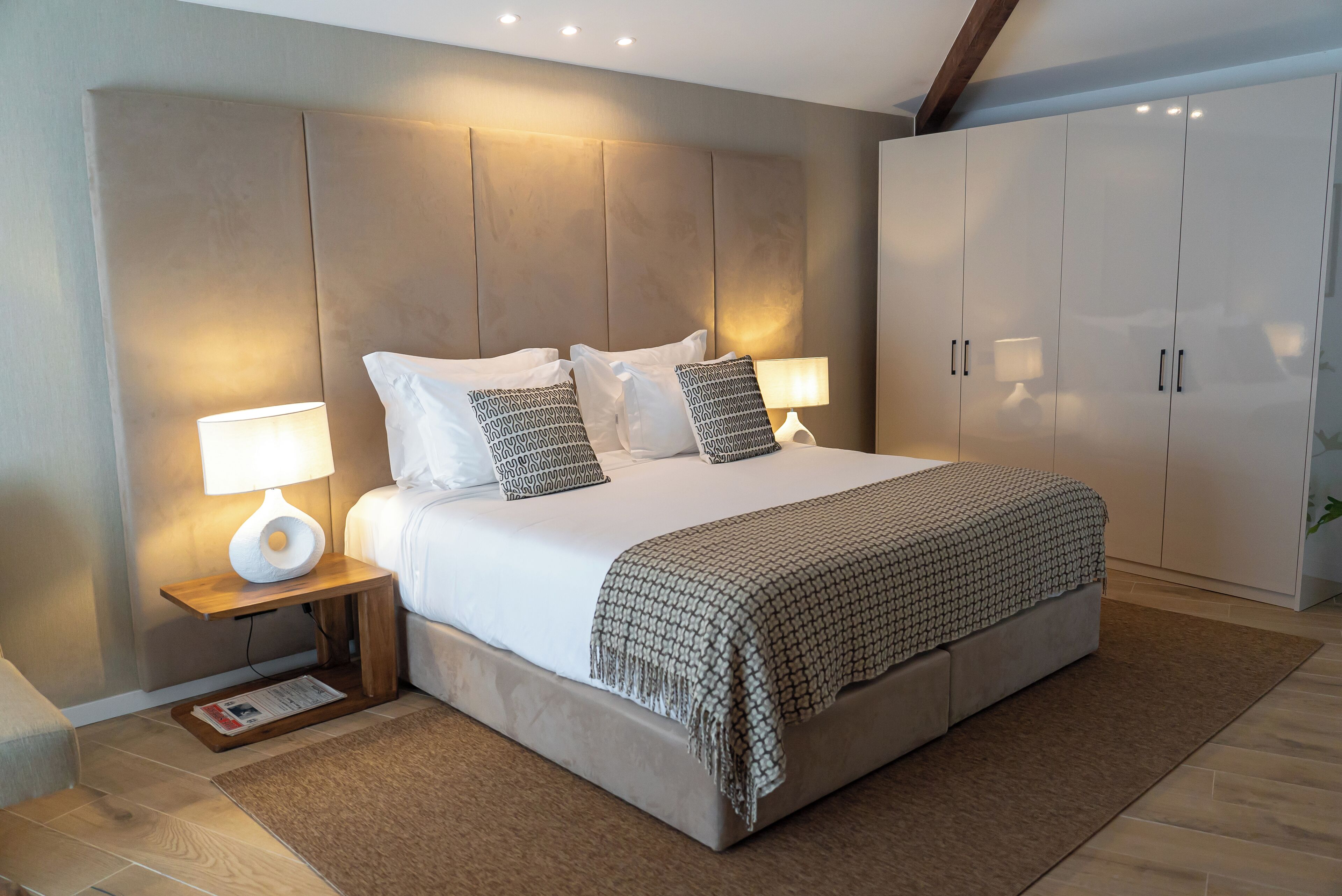 Quarto com uma cama grande, duas mesas de cabeceira com luminárias, um guarda-roupa e um painel de cama de madeira.