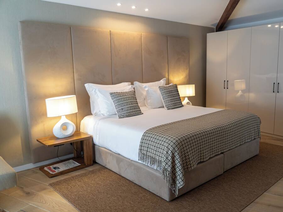 Quarto com uma cama grande, duas mesas de cabeceira com luminárias, um guarda-roupa e um painel de cama de madeira.