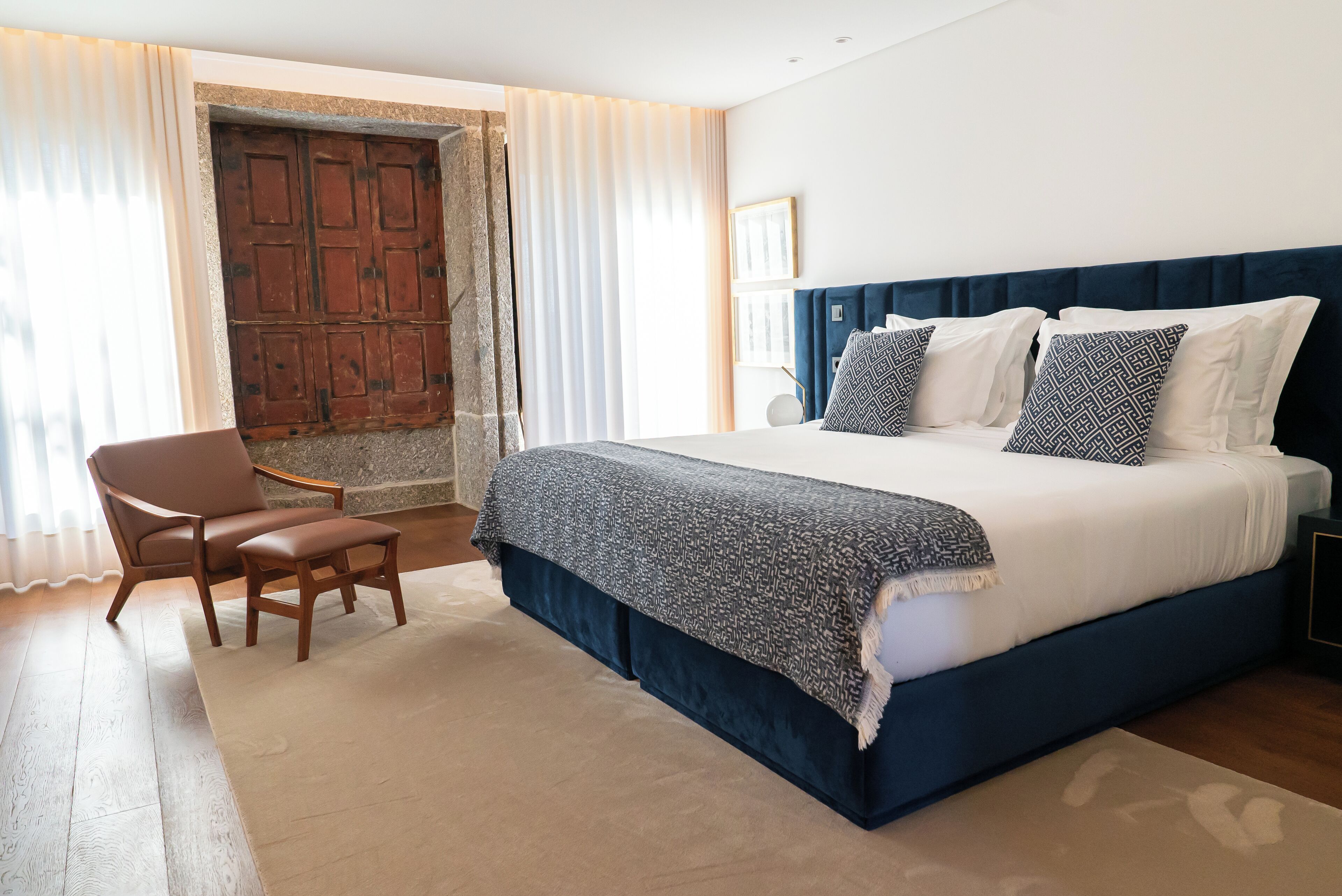 A bedroom with a large bed, a chair, a desk, and a view of a wooden door.