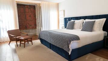 A bedroom with a large bed, a chair, a desk, and a view of a wooden door.