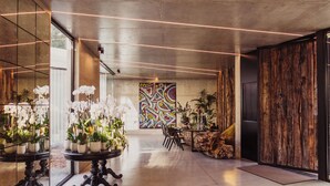 A modern lobby with a large mirror reflecting a floral arrangement, a colorful abstract painting, and a rustic wooden wall. - Quinta de Silvalde (Santo Tirso)