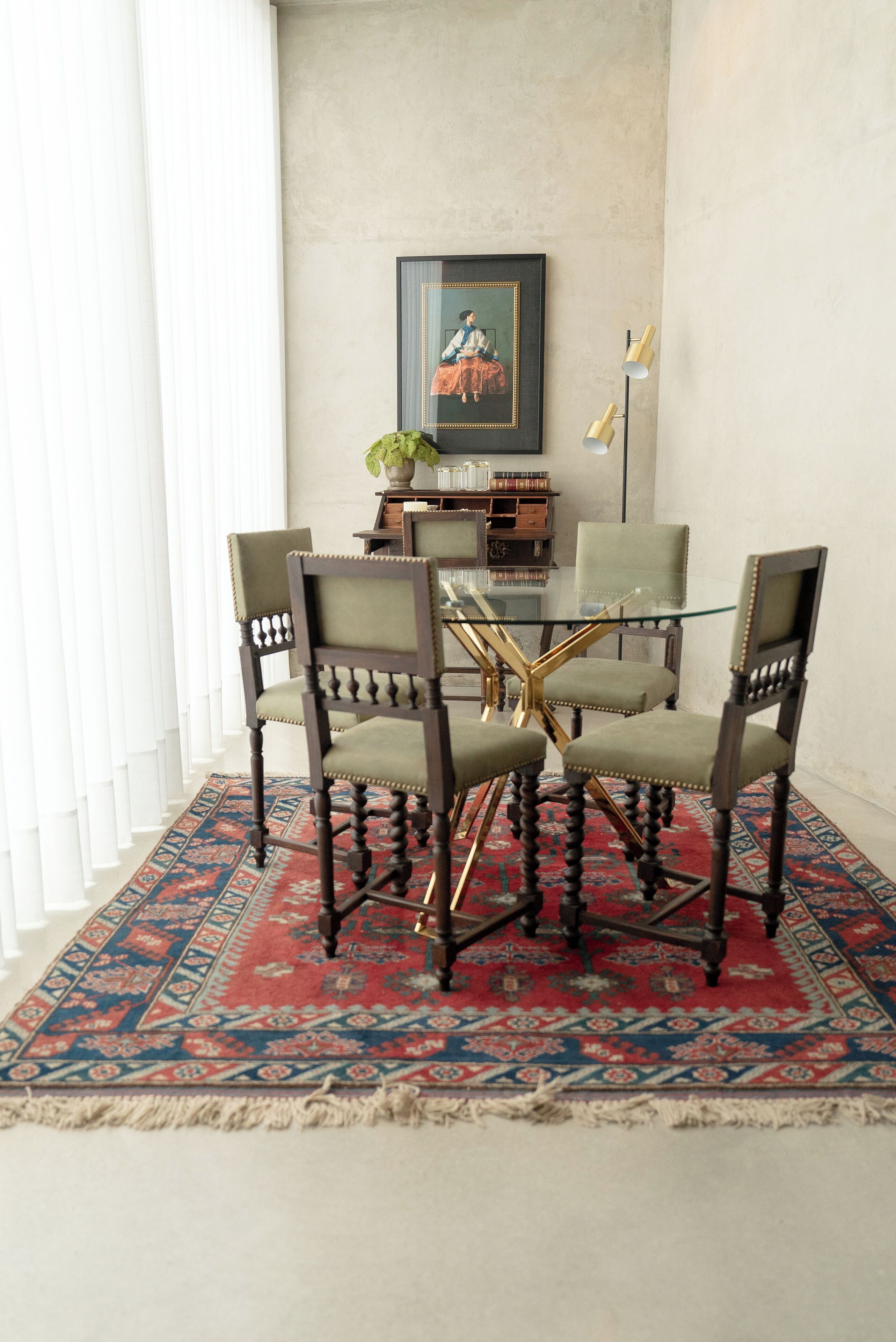 Zona pranzo con tavolo in vetro circondato da quattro sedie, tappeto decorato, libreria e quadro appeso al muro.