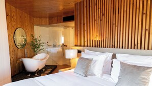 A modern hotel room with a wooden ceiling, a large bed with white linens, a white bathtub, and a mirror on the wall. - Quinta de Silvalde (Santo Tirso)