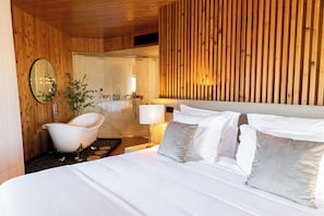 Habitación de hotel moderna con techo de madera, una cama grande con ropa blanca, una bañera blanca y un espejo en la pared.