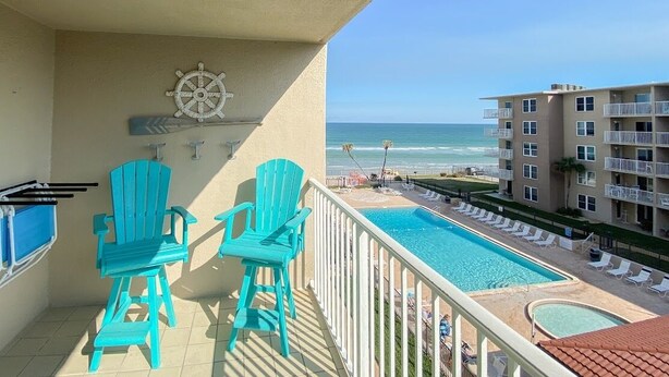 Un balcon avec deux chaises turquoise, une piscine et une vue sur l’océan.