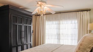 Une chambre avec un grand lit, un ventilateur de plafond et une armoire.