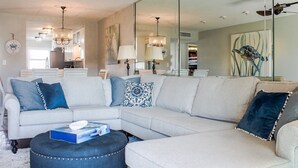 Un salon moderne avec un canapé d’angle, un pouf et une table à manger.