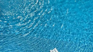 Ein klares, blaues Schwimmbecken mit einer weißen Liege und einer Holzterrasse.