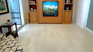 Ein Wohnzimmer mit Flachbildfernseher, Holzböden, einer Couch und einer Deckenleuchte.