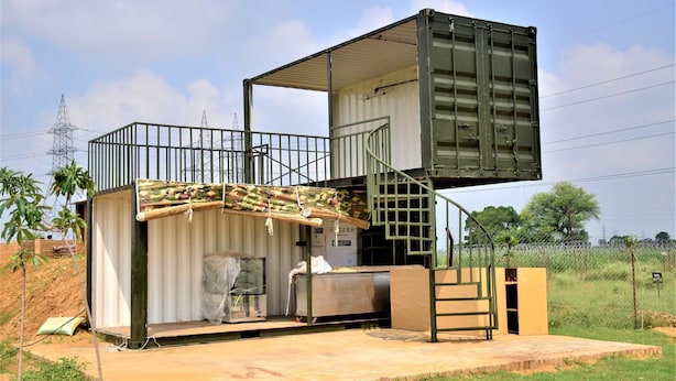 Edificio modular con una escalera, un espacio exterior cubierto y una barandilla metálica.