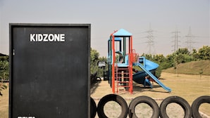 Un parque infantil con tobogán y estructura para escalar, rodeado por una cerca y un contenedor negro identificado como 'KIDZONE'.