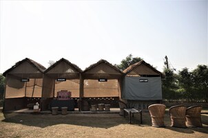 Three small, thatched-roof structures labeled "CHAKI," "BIOSCOP," and "MEHNDI," with wicker chairs in front.