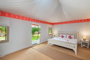 A bedroom with a white bed, two bedside tables, and a window with a view of greenery.