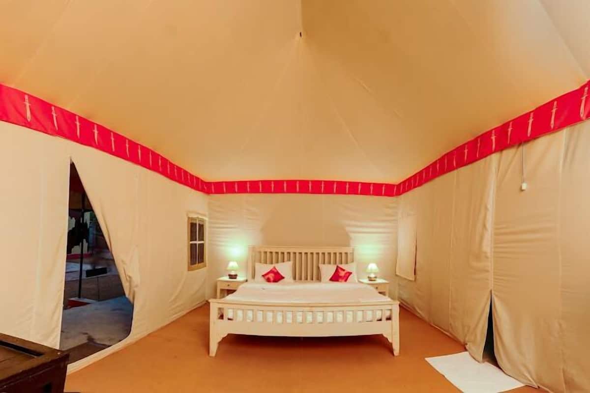 A tented room with a bed, two bedside lamps, and a window.