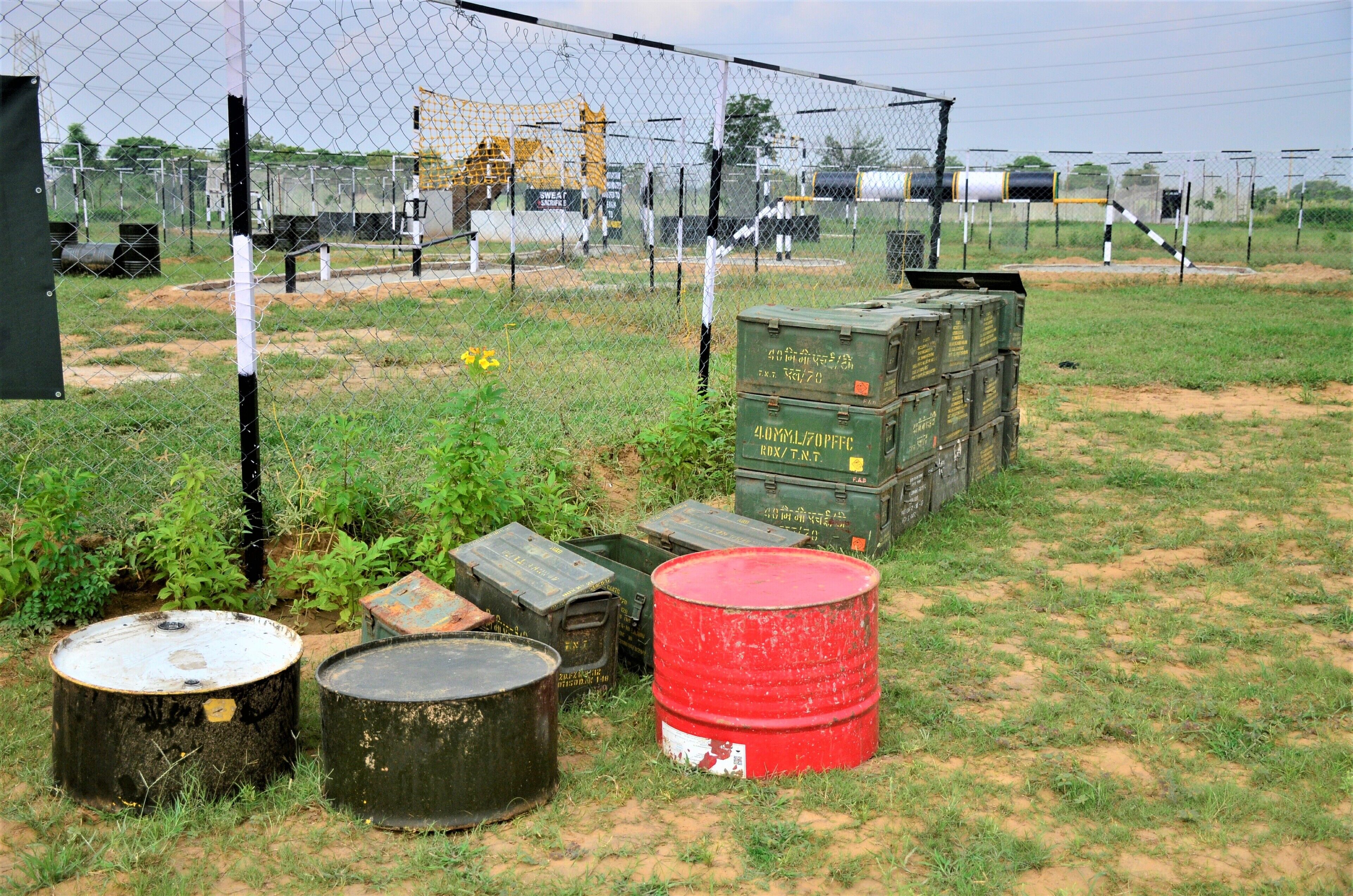 A fenced area with green shipping containers and barrels.