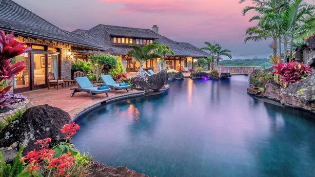 Een resort met een zwembad, ligbedden en tropische beplanting.