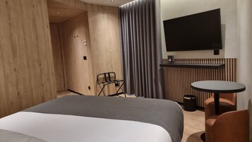 A hotel room with a bed, a small table, a chair, a TV, and a curtain.