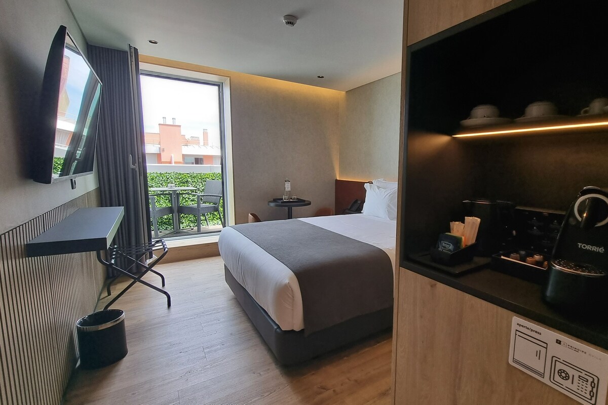 A hotel room with a bed, a desk, a chair, a coffee machine, and a TV.