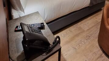 Quarto de hotel moderno com uma cama grande, mesa de cabeceira com telefone e televisão de tela plana na parede.