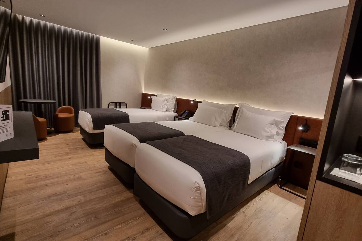 Une chambre d’hôtel avec deux lits, un bureau, une chaise, une petite table et une table de chevet avec une lampe.