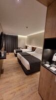 A modern hotel room with two beds, a desk, and a minibar.