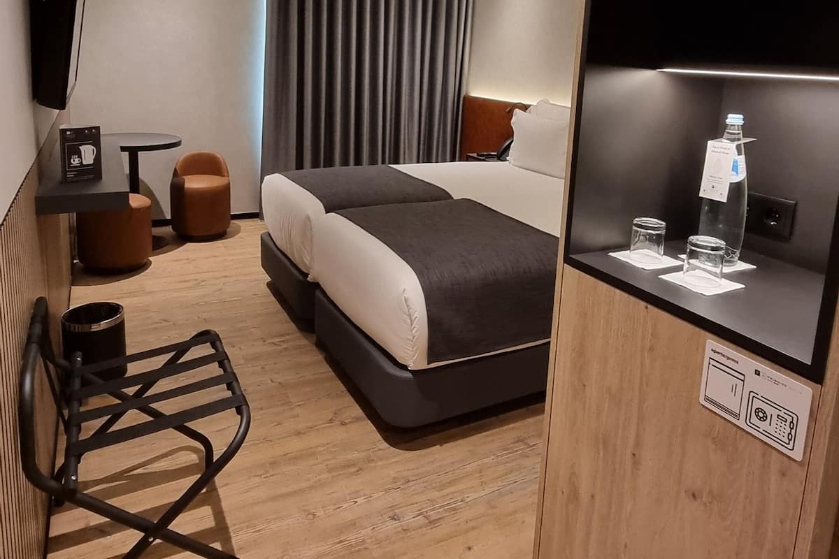 Une chambre d’hôtel moderne équipée d’un lit, d’un bureau, d’une chaise, d’une télévision et d’un mini-bar.