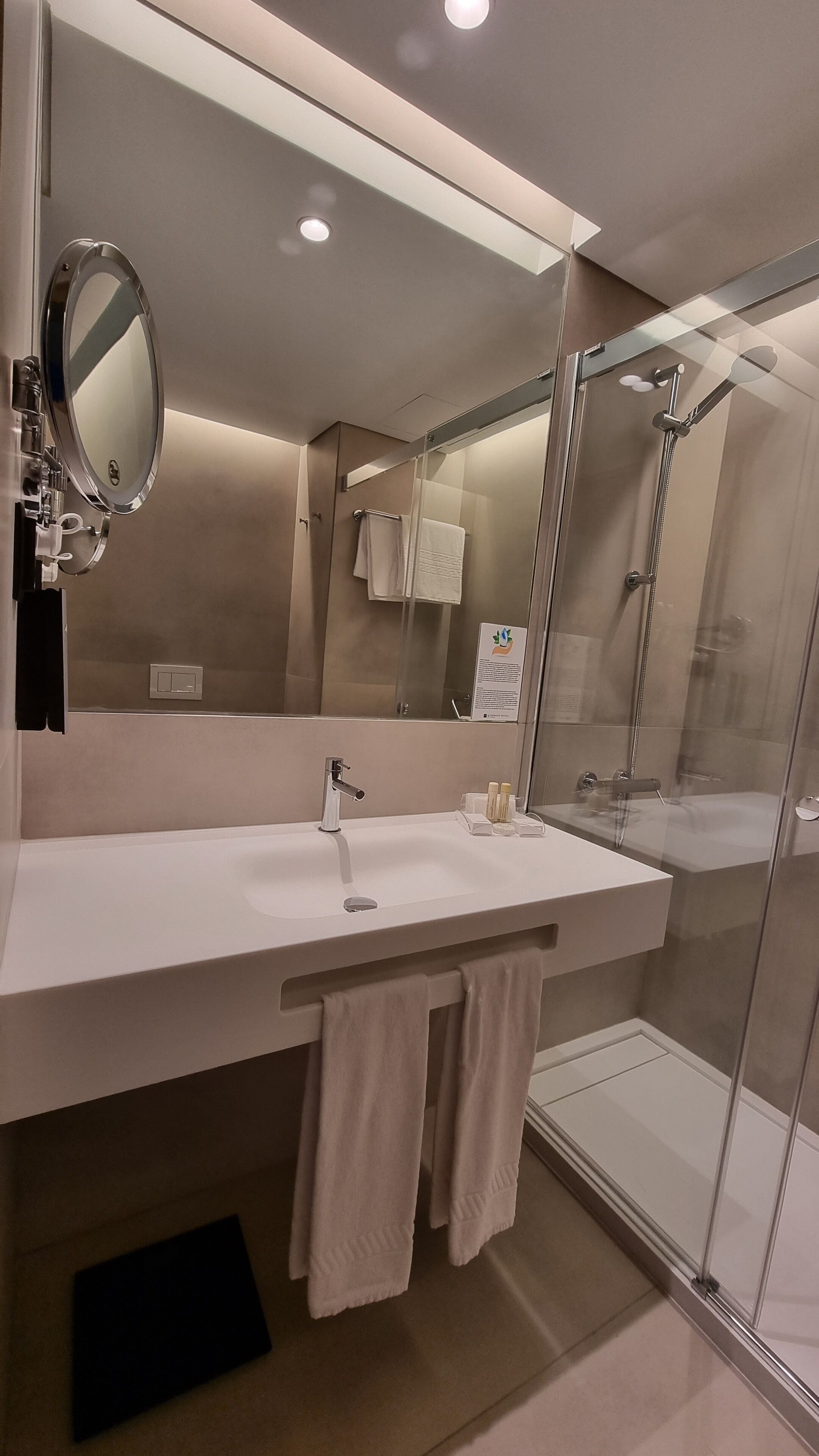 A modern bathroom with a large mirror, a sink, and a glass-enclosed shower.