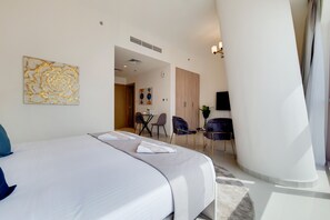 A hotel room with a large bed, a seating area with chairs, and a dining table. - GreenFuture - High-Rise Sleek Studio With Panoramic City Views (Dubai)