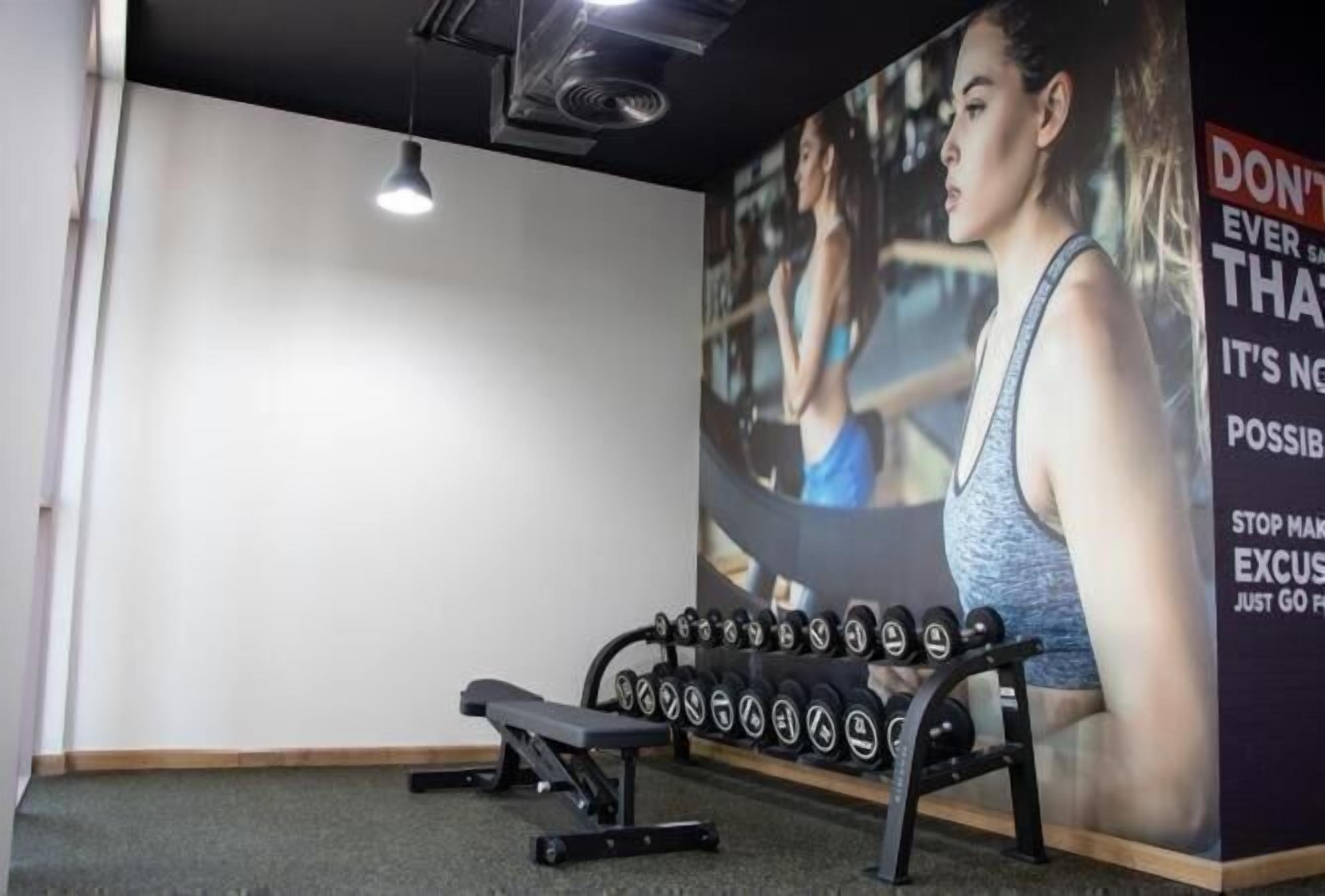 Un gimnasio con una banca, mancuernas y un cartel motivacional.