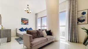 Un salon moderne avec un canapé beige, un lit gris et une grande fenêtre avec des rideaux.