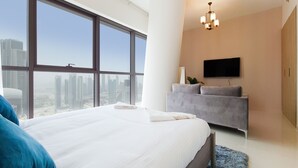 Une chambre moderne avec une grande fenêtre, un lit, un canapé gris et un téléviseur à écran plat.