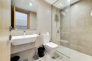 Un baño moderno con lavamanos, inodoro y zona de ducha con mampara de vidrio.
