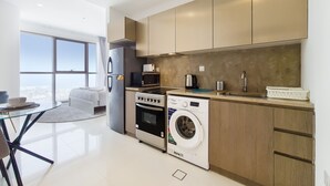A modern kitchen with stainless steel appliances, a built-in washer, and a large window offering a city view. - GreenFuture - Luxe Studio In Trade Center With Downtown Views (Dubai)