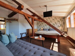 Ein gemütliches Zimmer mit einem Bett, einem Schlafsofa, einem kleinen Tisch und einem an der Decke befestigten Fernseher.