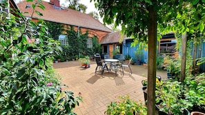 Eine Terrasse mit Backsteinboden, umgeben von Topfpflanzen und einem Tisch mit Stühlen.