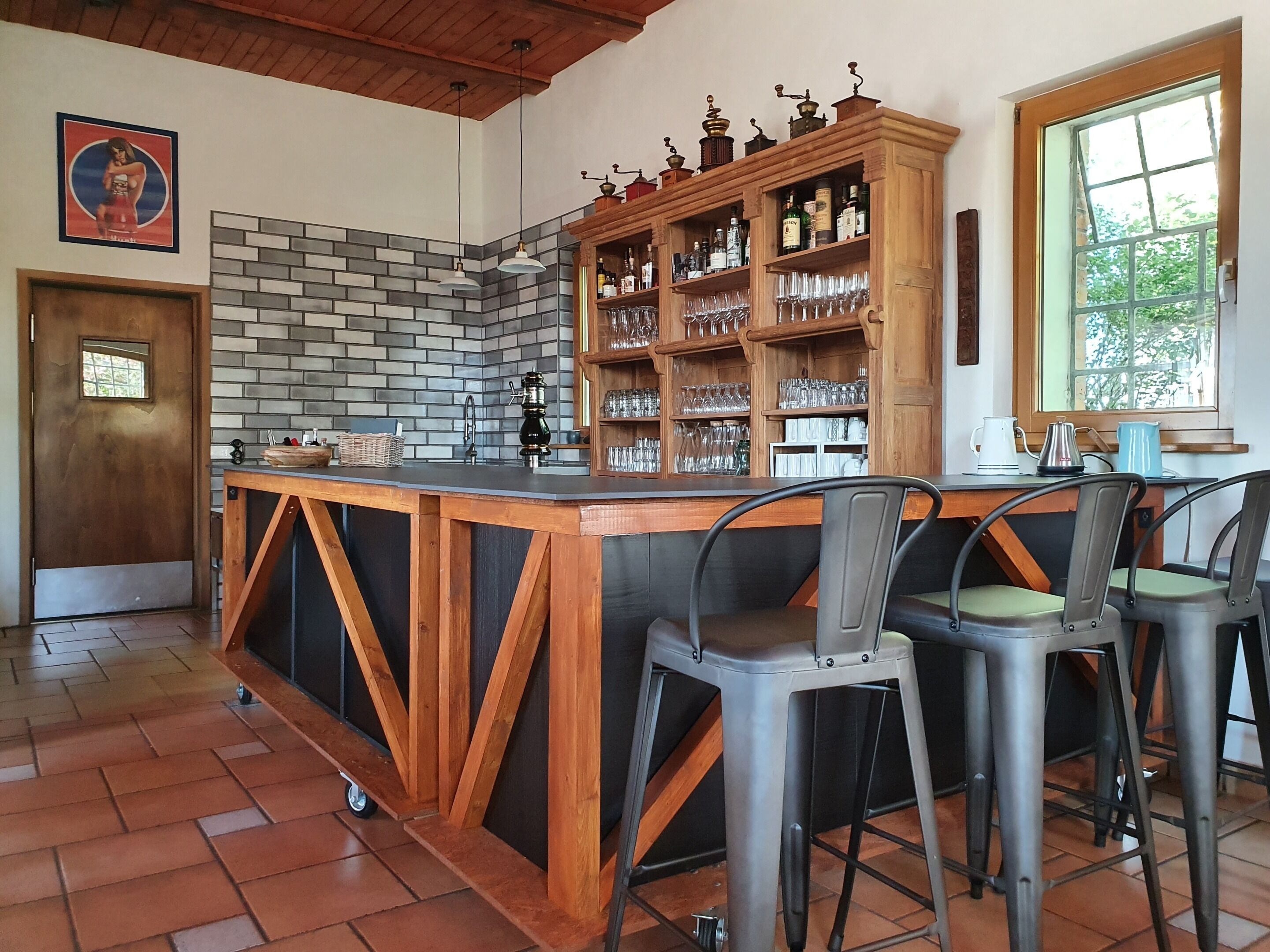 A bar area with a brick wall backsplash, wooden shelves with glasses, and a door with a window.