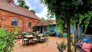 A brick building with a patio area featuring tables and chairs, a barbecue grill, and potted plants. - Single room-#9 LütunLüt NEU im EG-Standard-Ensuite with Bath (Groß Dratow)