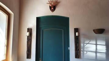 A teal door with a decorative antler mounted above it, flanked by two wall-mounted sconces.