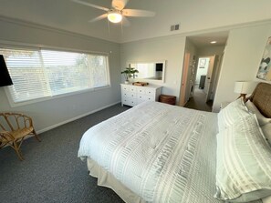 A bedroom with a large bed, a ceiling fan, a dresser, a chair, and a window with blinds.