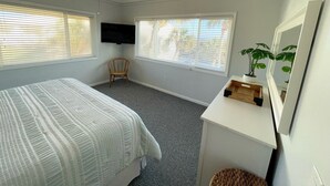 Una camera da letto con un letto, una sedia, una scrivania con uno specchio e una televisione appesa al muro.