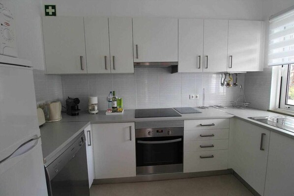 Una cocina moderna con armarios blancos, electrodomésticos de acero inoxidable y un ventanal que proporciona luz natural.