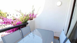 Ein Balkon mit Glastisch und Stühlen, umgeben von leuchtend rosa Blüten.