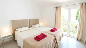 Ein Hotelzimmer mit zwei Betten, einem Nachttisch und einer Schiebeglastür zum Außenbereich.