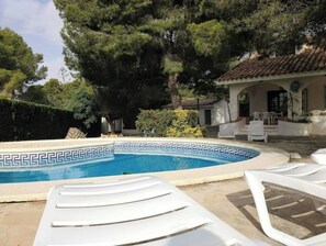 A swimming pool with a decorative edge, surrounded by lounge chairs and a building with a tiled roof.