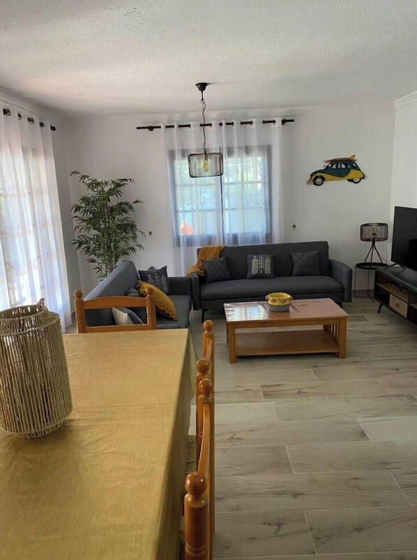 A living room with a sofa, a coffee table, a dining table with chairs, a lamp, and a decorative car on the wall.