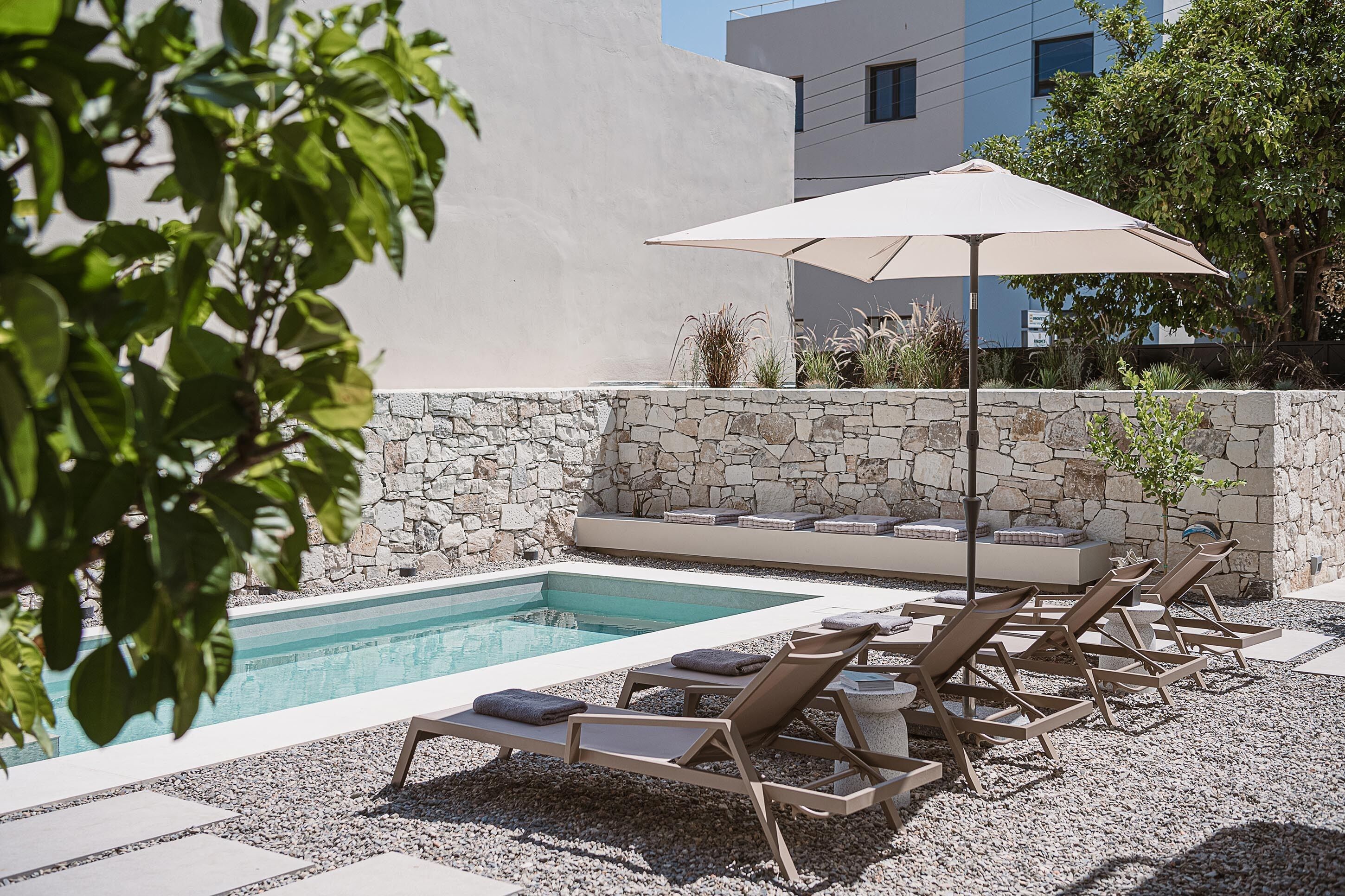 Un espace aménagé au bord de la piscine, avec des chaises longues, un mur en pierre et un parasol.