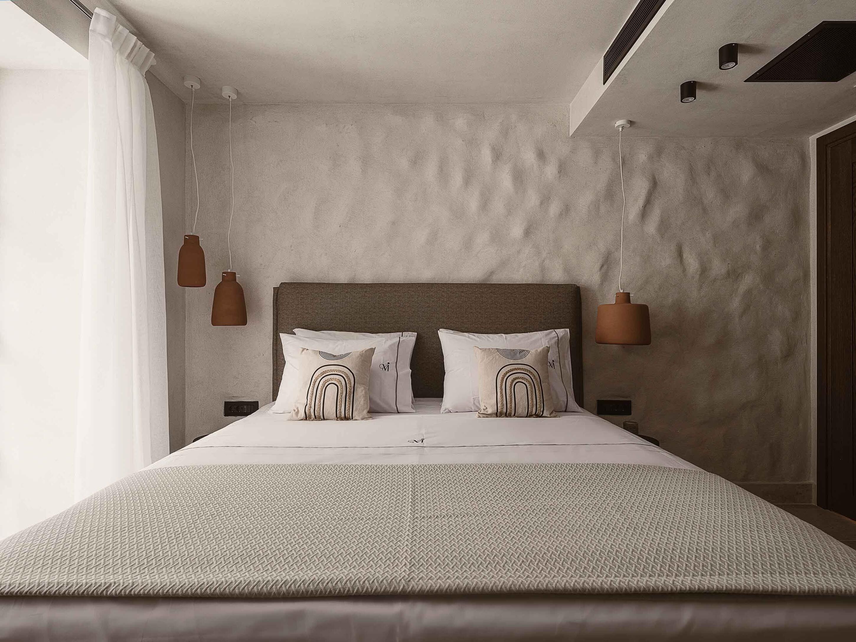 A modern bedroom with a large bed, two bedside tables, and pendant lights.