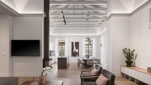 A spacious living room with a modern design, featuring a large flat-screen TV, a wooden coffee table, and comfortable seating.