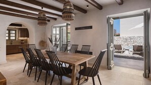 A spacious dining area with a wooden table and black chairs, a kitchen with a window, and a view of a pool through an open door.